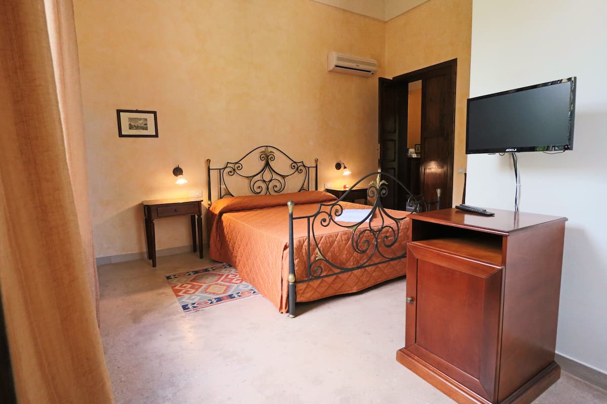 Quarto com cama, mesa de cabeceira, luminária, televisão, guarda-roupa e um tapete pequeno.