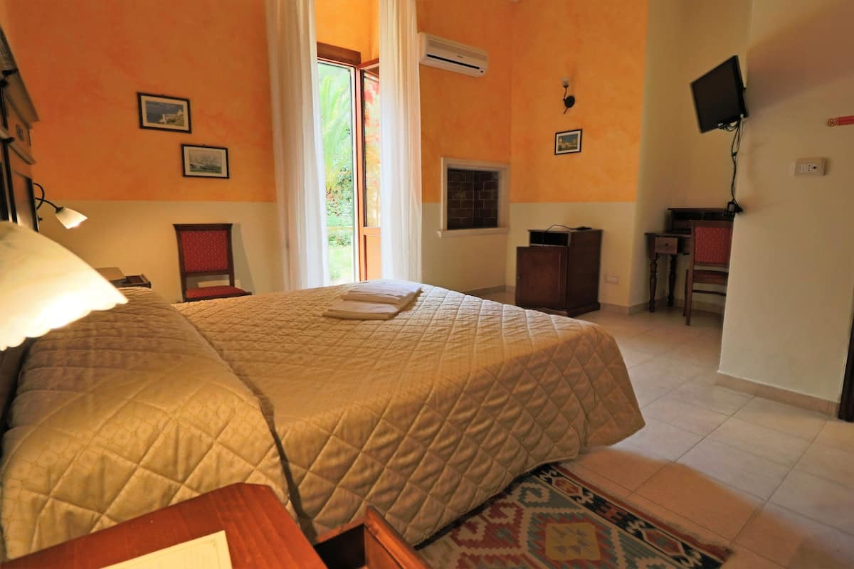 Quarto com cama, escrivaninha, cadeira e televisão na parede.
