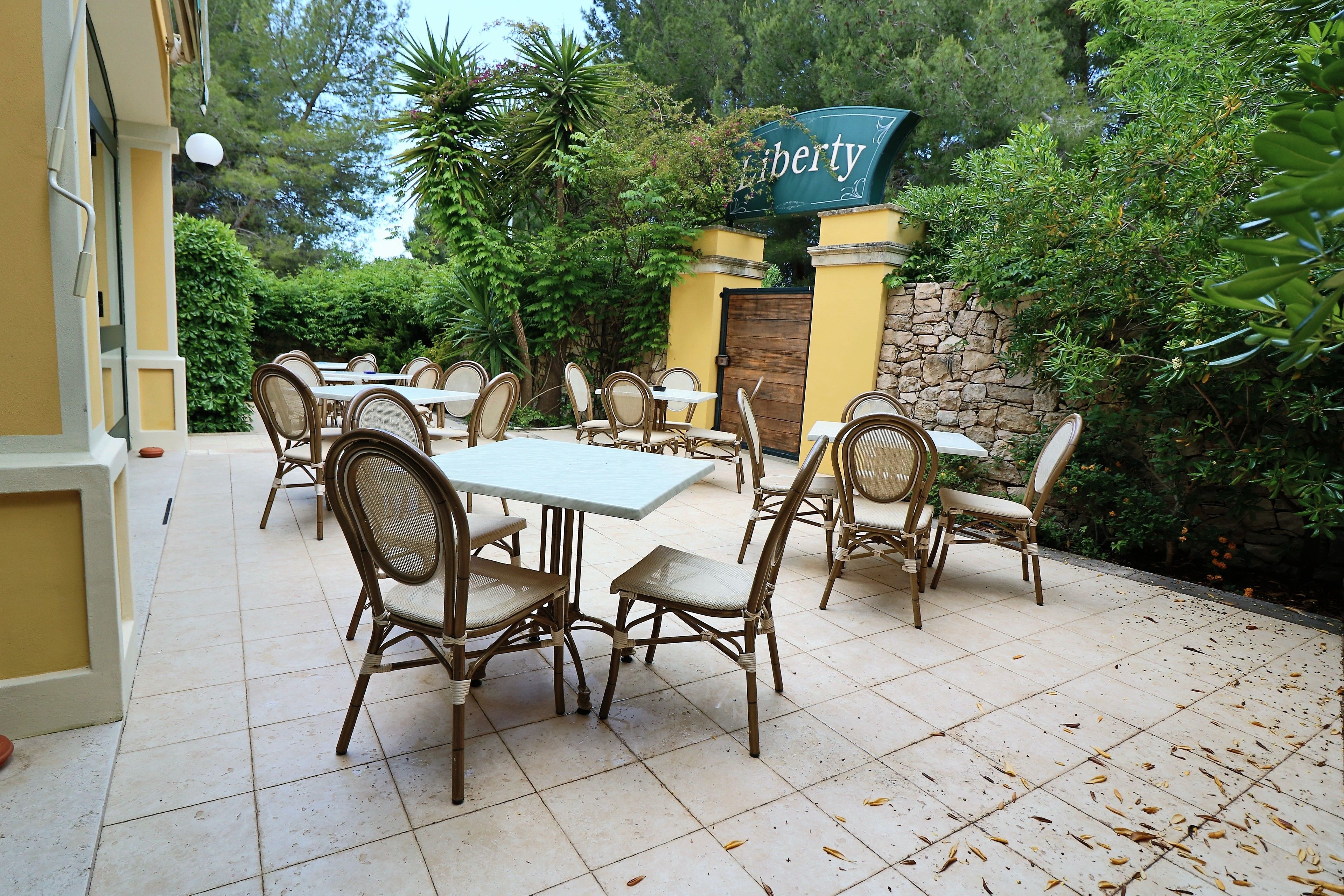 An outdoor patio with tables and chairs, surrounded by greenery and a stone wall.