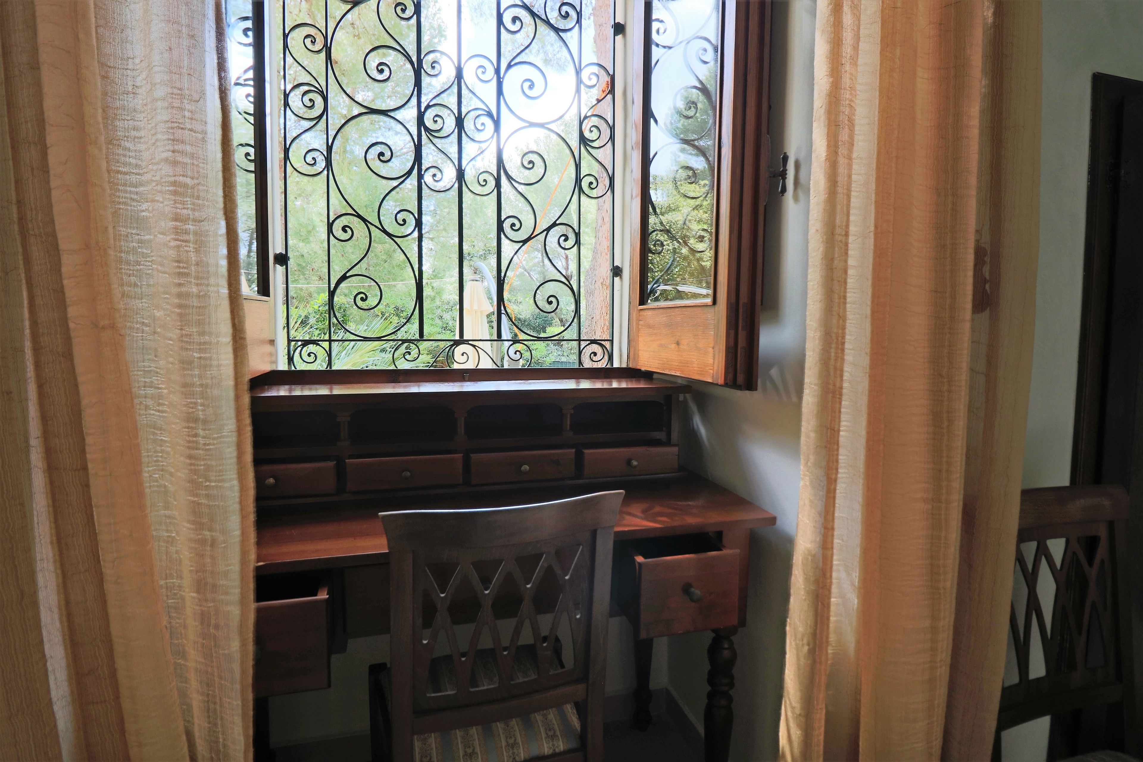 A study area with a wooden desk, a chair, and a window with decorative iron bars.