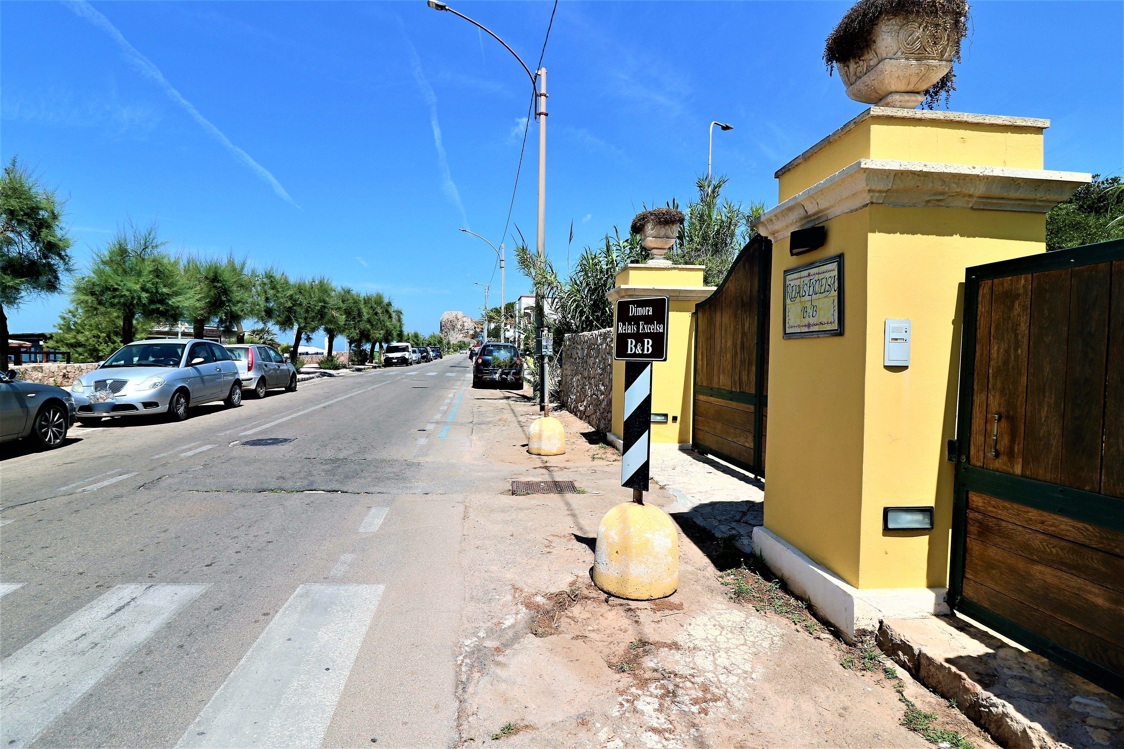 A street view with a yellow building, a wooden gate, and a sign indicating a B&B.