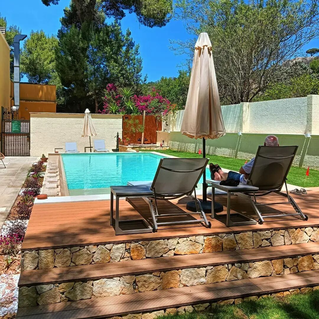 A pool area with lounge chairs, a stone pathway, and a view of the surrounding garden.