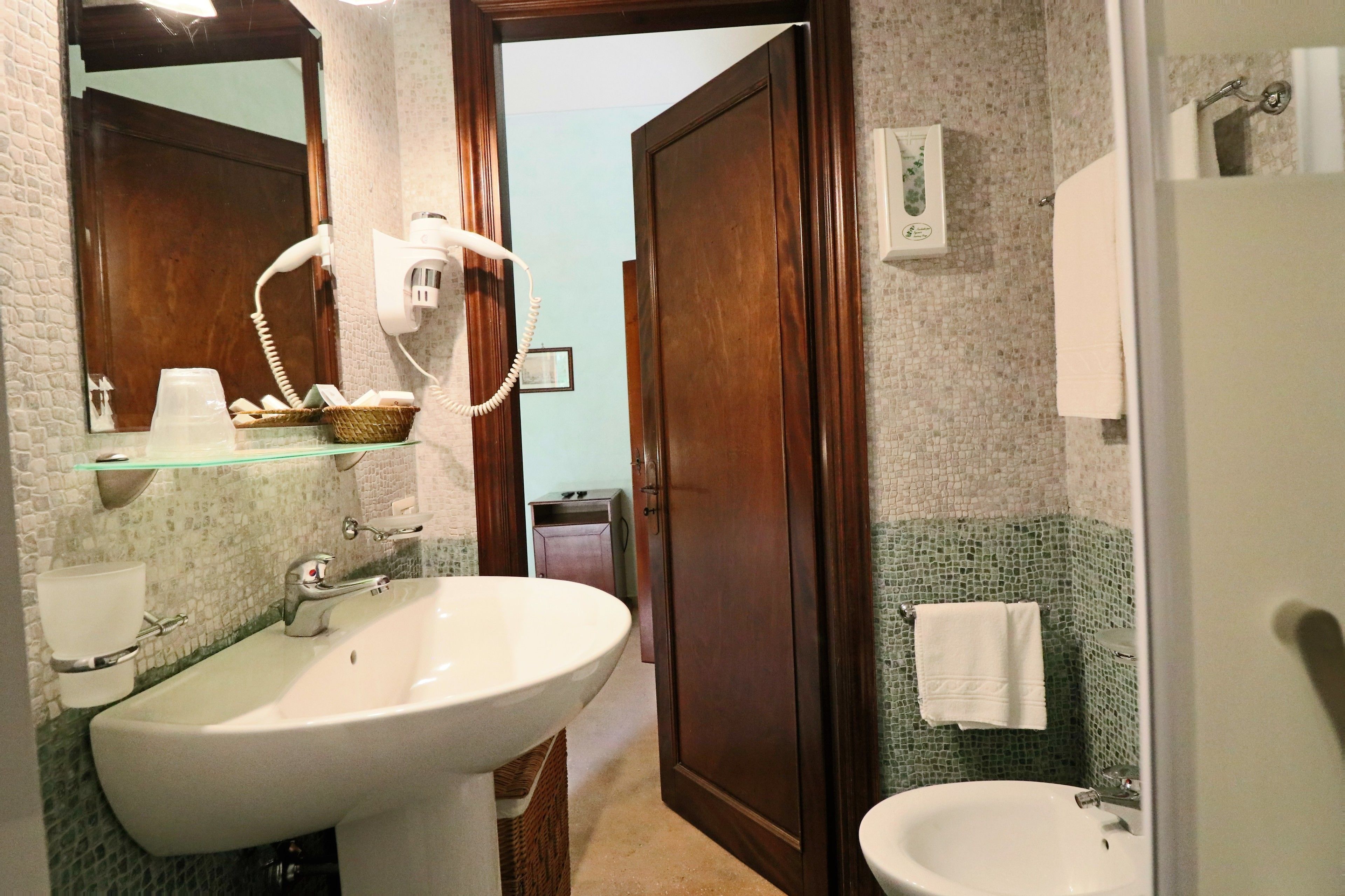 Une salle de bain avec un grand lavabo, un miroir, un sèche-cheveux et une petite fenêtre.