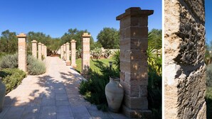 A pathway flanked by stone pillars and large vases, leading through a garden with cacti and trees. - Masseria L'Uliveto (Otranto)