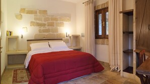 A bedroom with a bed, a stone wall, a window, and a table with a lamp. - Masseria L'Uliveto (Otranto)
