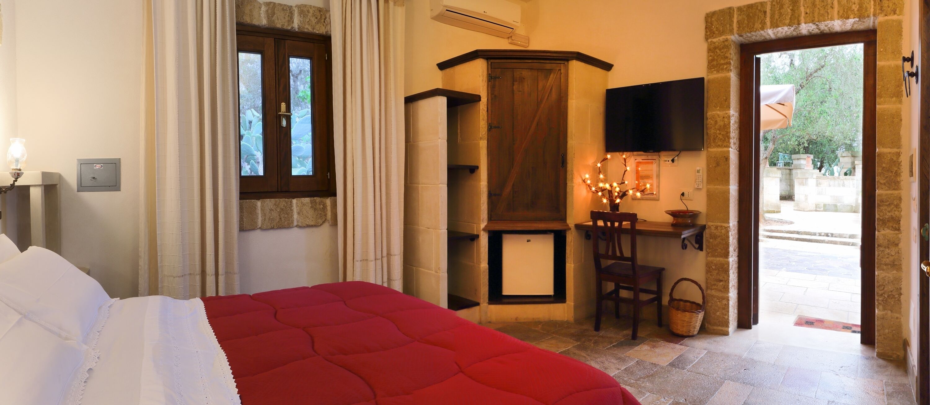 A hotel room with a bed, a television, a small table with a chair, and a stone wall.