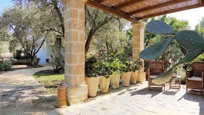 A garden patio with stone flooring, potted plants, and wicker furniture under a pergola. - Masseria L'Uliveto (Otranto)