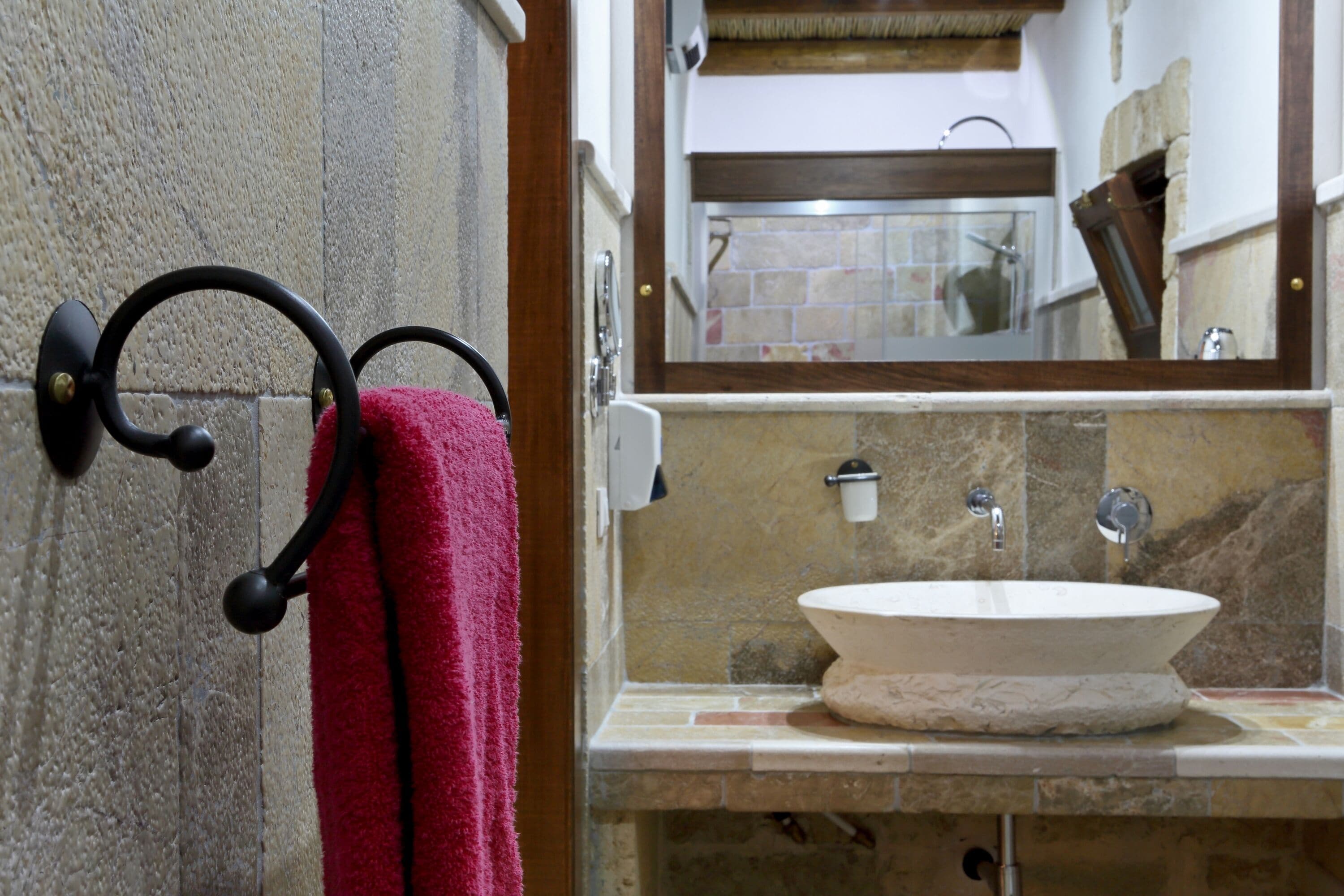 A bathroom with a stone sink, a mirror, and a towel rack with a red towel.