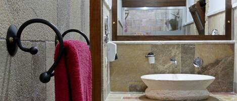 A bathroom with a stone sink, a mirror, and a towel rack with a red towel.