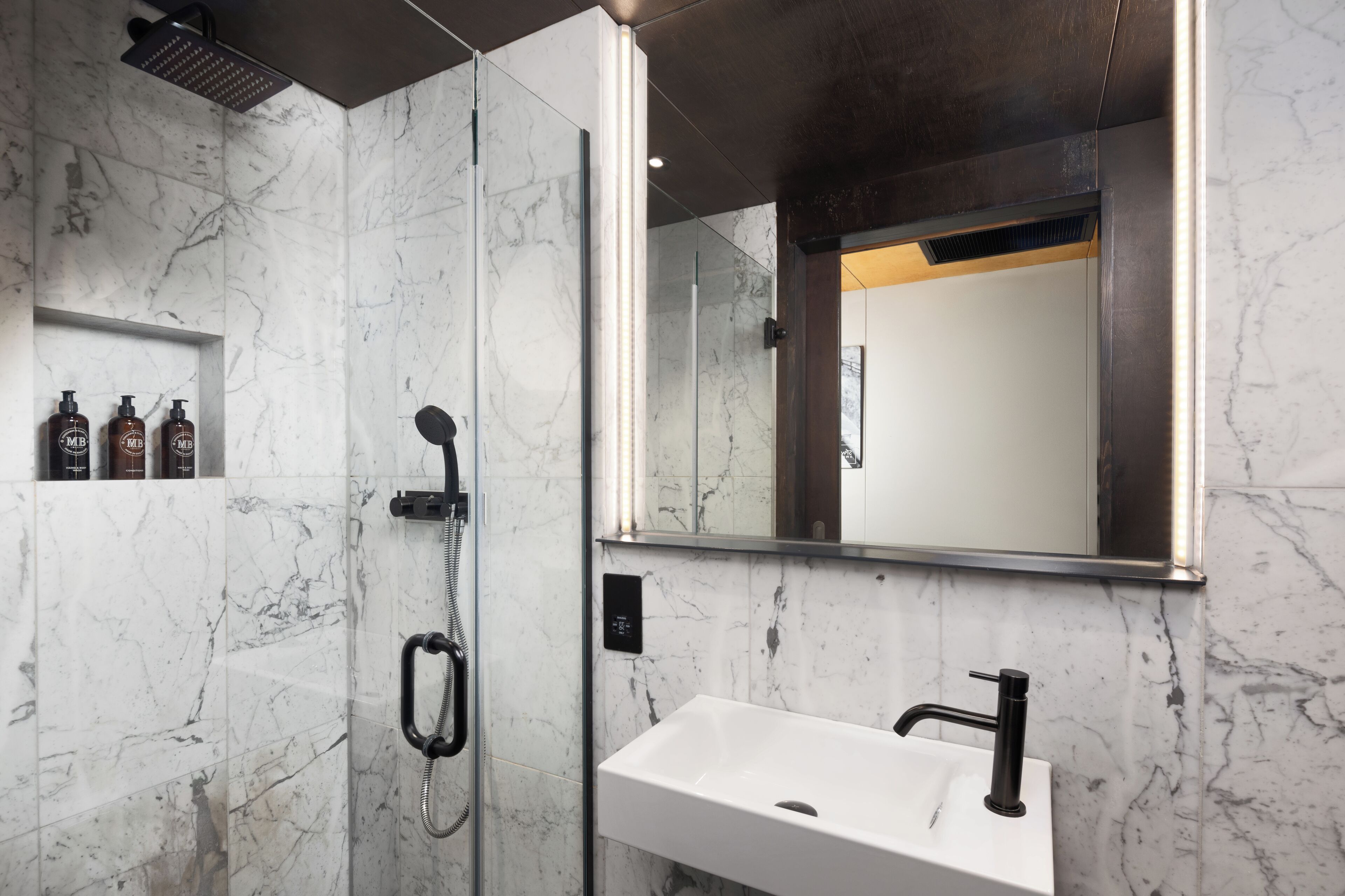 A modern bathroom with a marble shower, a white sink, and a large mirror.