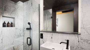 A modern bathroom with a marble shower, a white sink, and a large mirror.
