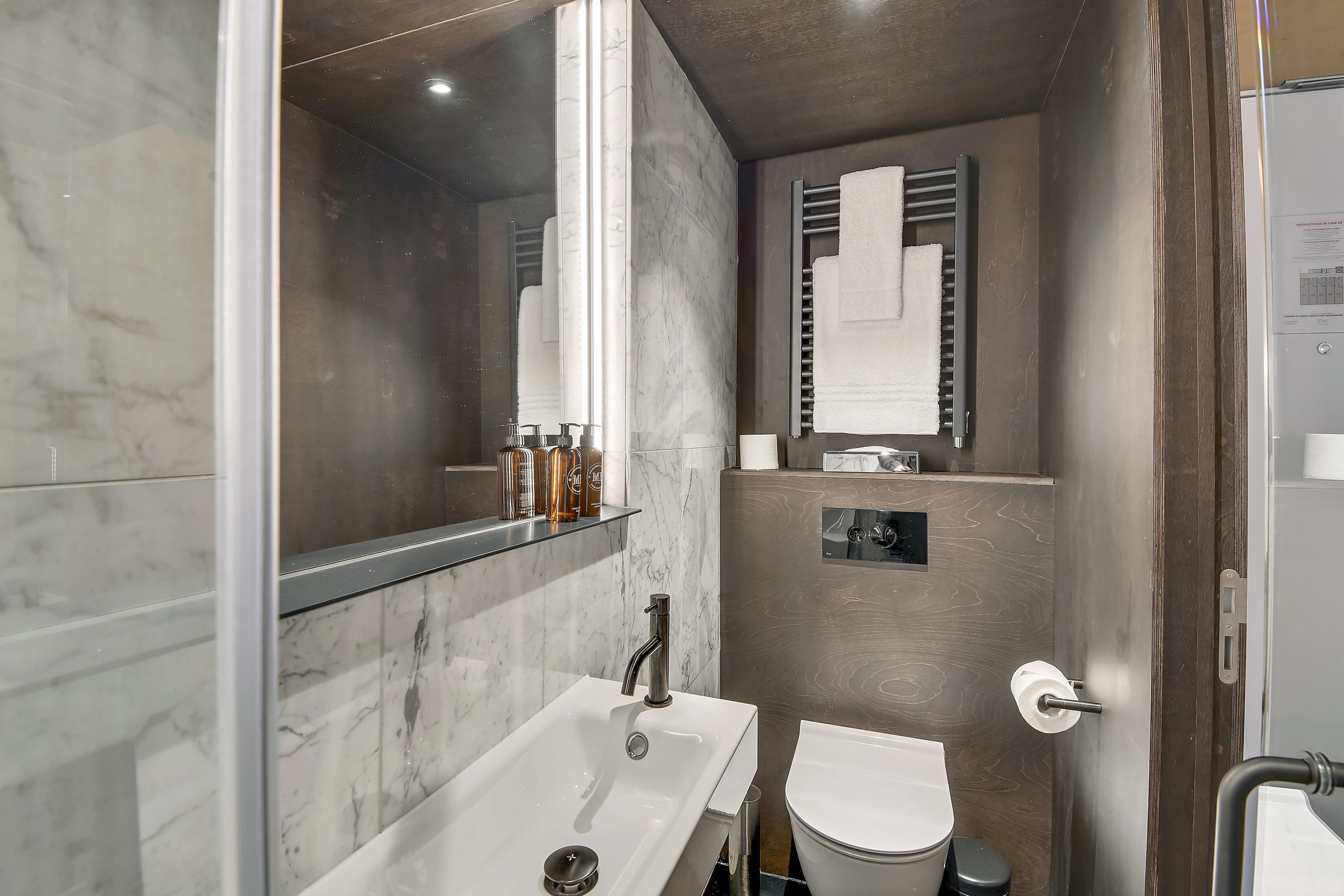 A modern bathroom with a marble sink, a toilet, and a glass shower enclosure.