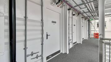 Un pasillo con puertas blancas, barandillas de metal y alfombra gris.