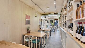 A restaurant with wooden tables and chairs, a wine shelf, and hanging pendant lights.