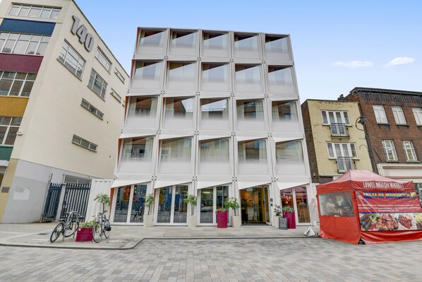A modern building with a glass facade and a red tent advertising a food stall. - Stow Away Waterloo (London)