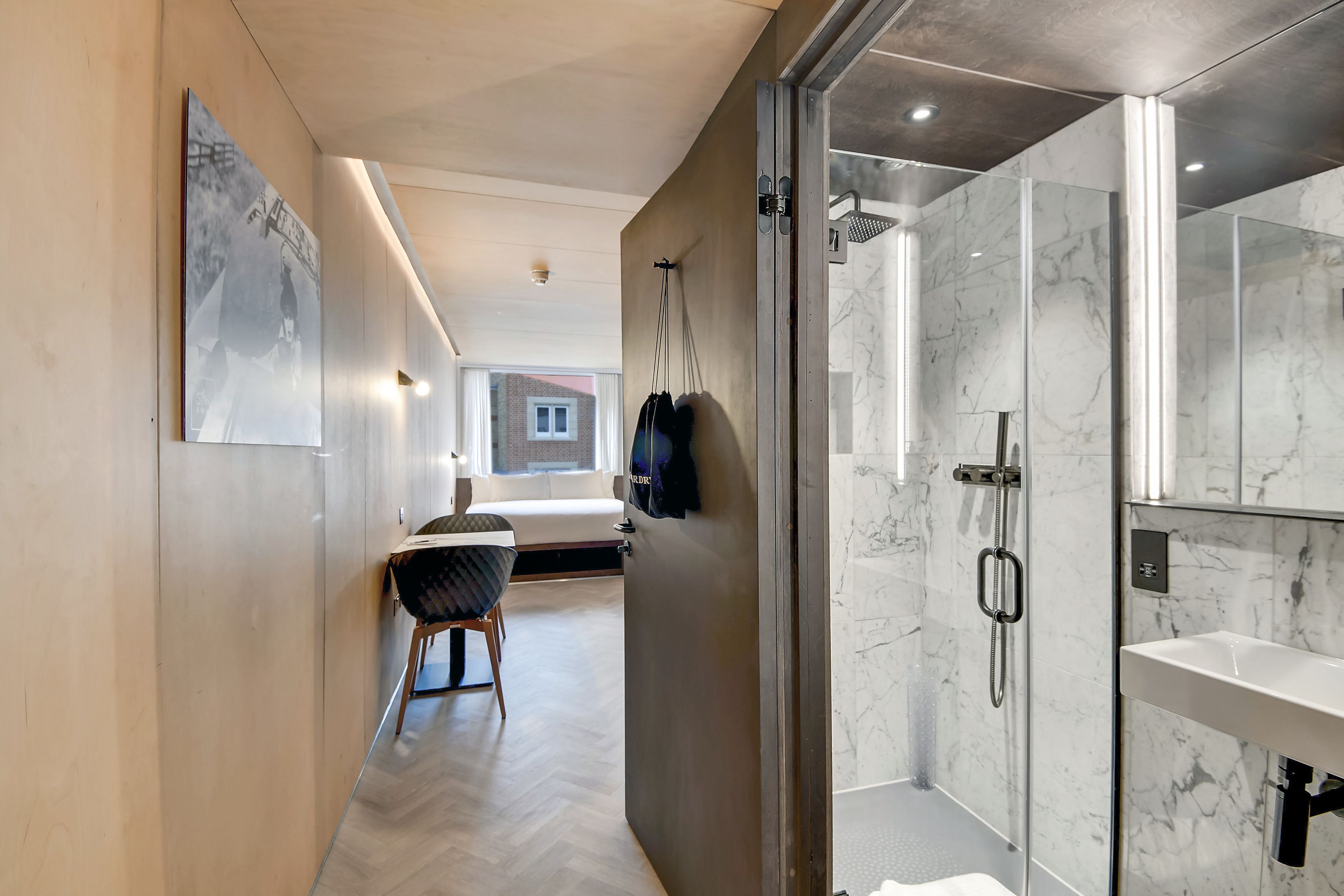 A modern bathroom with a glass shower enclosure, a marble-tiled wall, and a white sink.