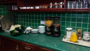 Una cocina con baldosas verdes, una cafetera, un cesto de pan y diversos utensilios de cocina.