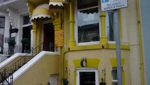Un edificio amarillo con una escalera que conduce a la entrada, un letrero que indica un área de estacionamiento y un cartel de hotel visible al fondo.