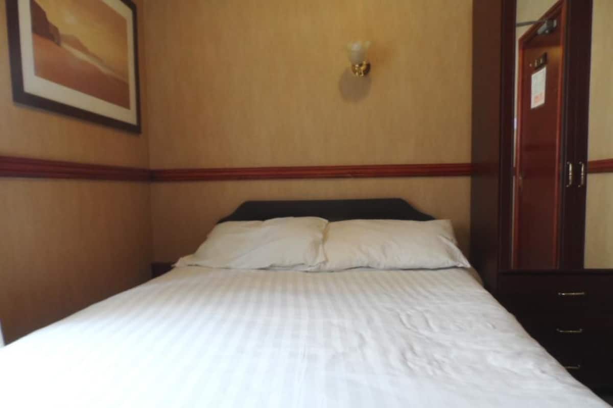 A hotel room with a bed, a wall-mounted light fixture, and a door with a sign.