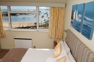 Habitación de hotel con un ventanal que ofrece vistas a barcos y a la playa.