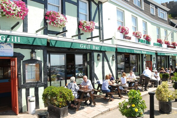 A traditional building with a 'Grill Bar' and 'Dolphin Hotel' signs, featuring outdoor seating and flower boxes. - The Dolphin Hotel (St. Martin)