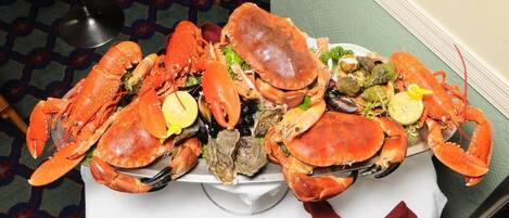 A table with a large platter of cooked crabs and oysters, a knife, and a napkin.