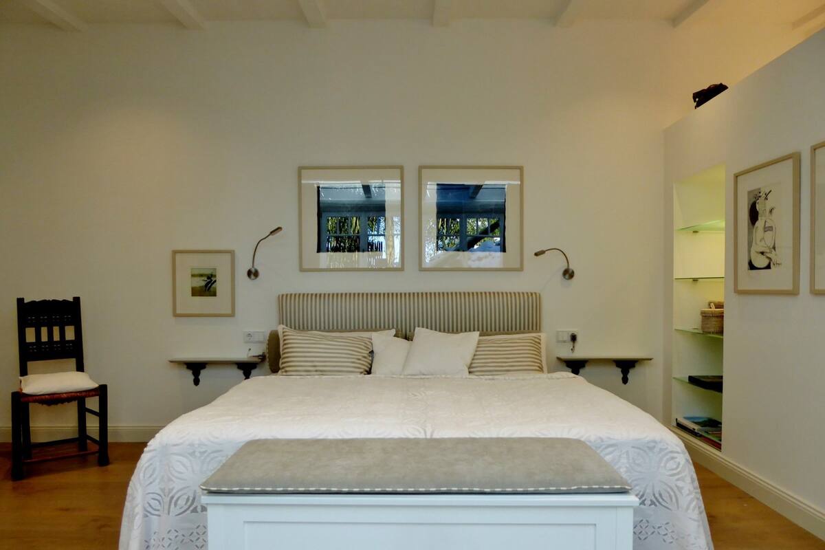 A bedroom with a large bed, two bedside tables, a chair, and artwork on the walls.