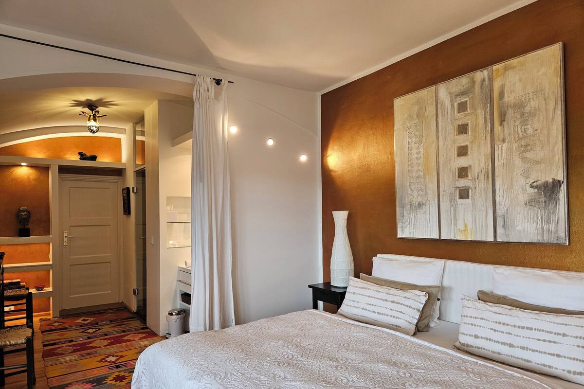 A hotel room with a large bed, a nightstand, a vase, and a painting on the wall.