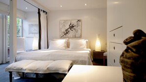 A modern bedroom with a large bed, a bedside table, a lamp, and a window with curtains. - Am Eichholz Galerie & Art Hotel (Murnau am Staffelsee)