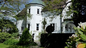 A white building with a green roof, surrounded by greenery and a statue. - Am Eichholz Galerie & Art Hotel (Murnau am Staffelsee)