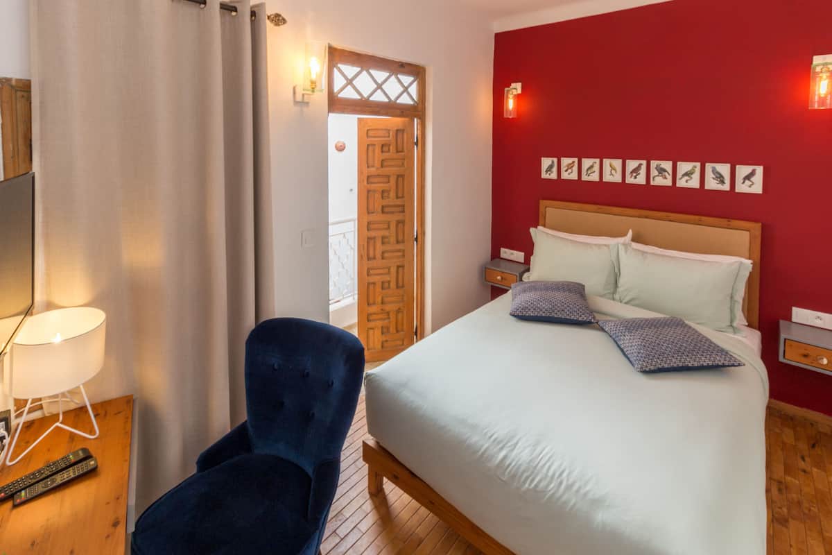 A bedroom with a bed, a chair, a lamp, and a door leading to another room.