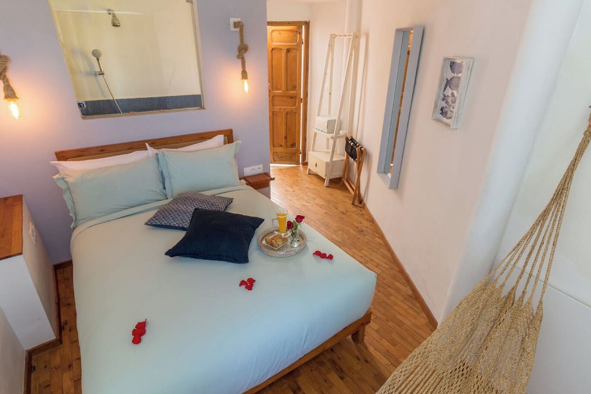 A bedroom with a bed, a wooden floor, a hammock, and a bathroom with a shower.