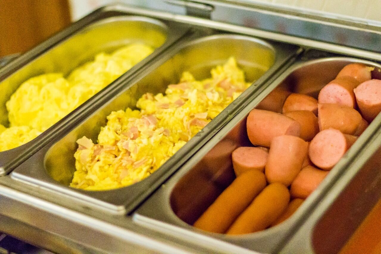 Un bufé con tres opciones de comida: huevos revueltos, un plato combinado con jamón y salchichas.