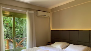 A hotel room with a bed, a nightstand, an air conditioning unit, and a view of greenery through a glass door. - Villa Flor Ecoresort (Nova Petropolis)