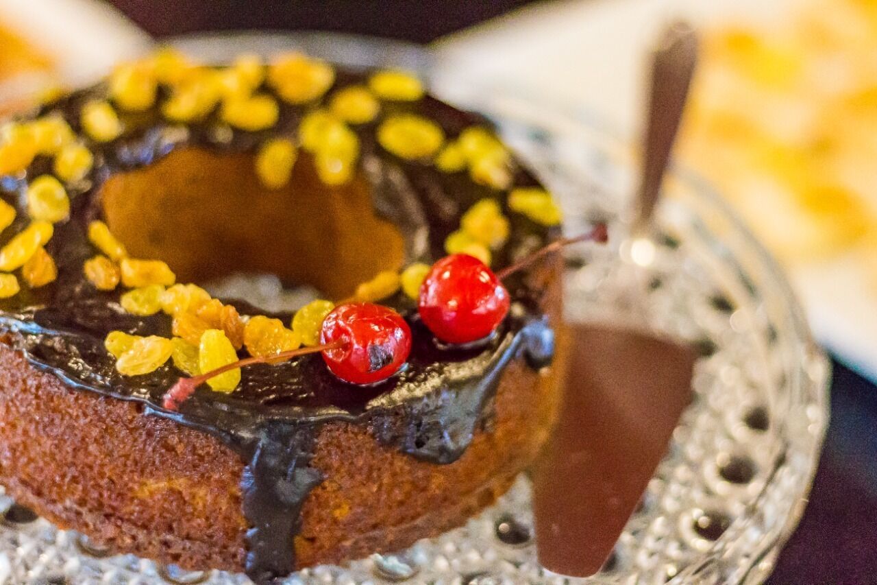Un donut glaseado de chocolate con fruta seca y cerezas sobre un plato decorativo.