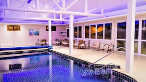 An indoor swimming pool with a blue tiled floor, white pillars, and a seating area with chairs and tables. - Villa Flor Ecoresort (Nova Petropolis)