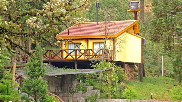 A yellow building with a red roof, a stone wall, and a waterfall. - Villa Flor Ecoresort (Nova Petropolis)