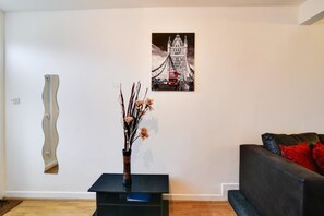 A living room with a black sofa, a black coffee table with a vase of dried flowers, and a framed picture of a bridge. - Two Bedroom Serviced Apartment (Luton)