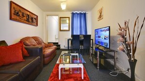 A living room with a leather sofa, a glass coffee table, a television, and a vase with flowers. - Two Bedroom Serviced Apartment (Luton)