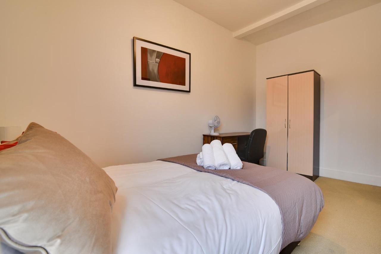 A hotel room with a bed, a desk, a chair, a wardrobe, and a framed picture on the wall.