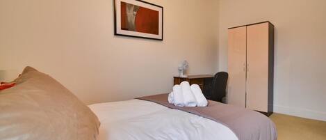 A hotel room with a bed, a desk, a chair, a wardrobe, and a framed picture on the wall.
