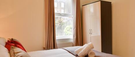 A hotel room with a bed, a wardrobe, and a window with curtains.