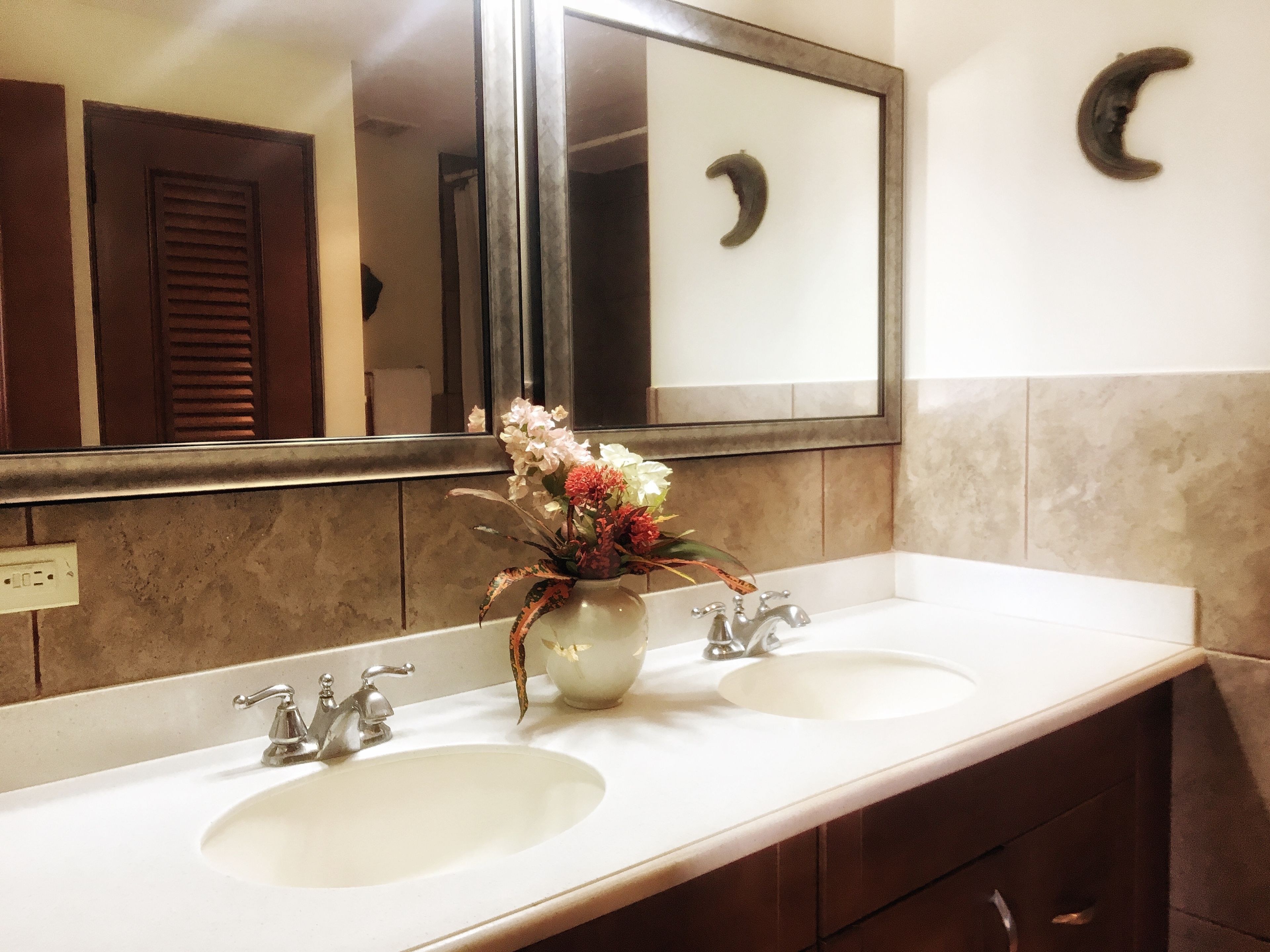 A bathroom with two sinks, a mirror, and a vase with flowers.