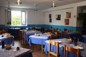 A dining area with tables covered in blue tablecloths, wooden chairs, and hanging light fixtures. - Hotel Ornella (Camaiore)