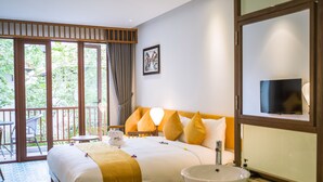 Hotelkamer met een bed, een badkamer met een wastafel, een televisie en een balkon met uitzicht op groen.
