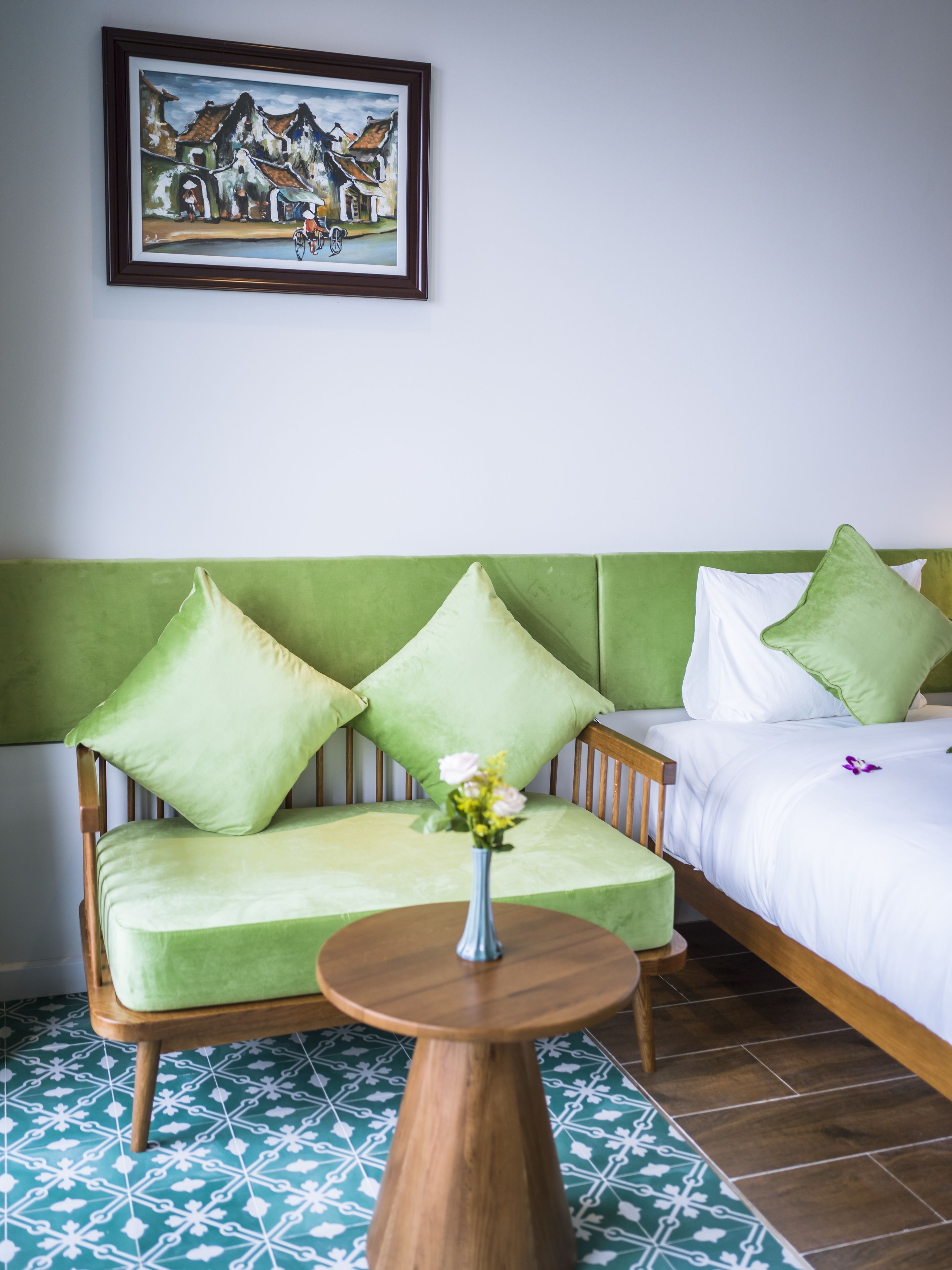 A room with a green sofa, a wooden chair, a small round table, and a bed with white bedding.