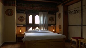 A traditional room with a wooden bed, two bedside lamps, and decorative wall plates. - AMA's Village Lodge (Paro)