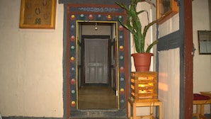 A hallway with a decorative door frame, a potted plant on a wooden stool, and a framed picture on the wall. - AMA's Village Lodge (Paro)