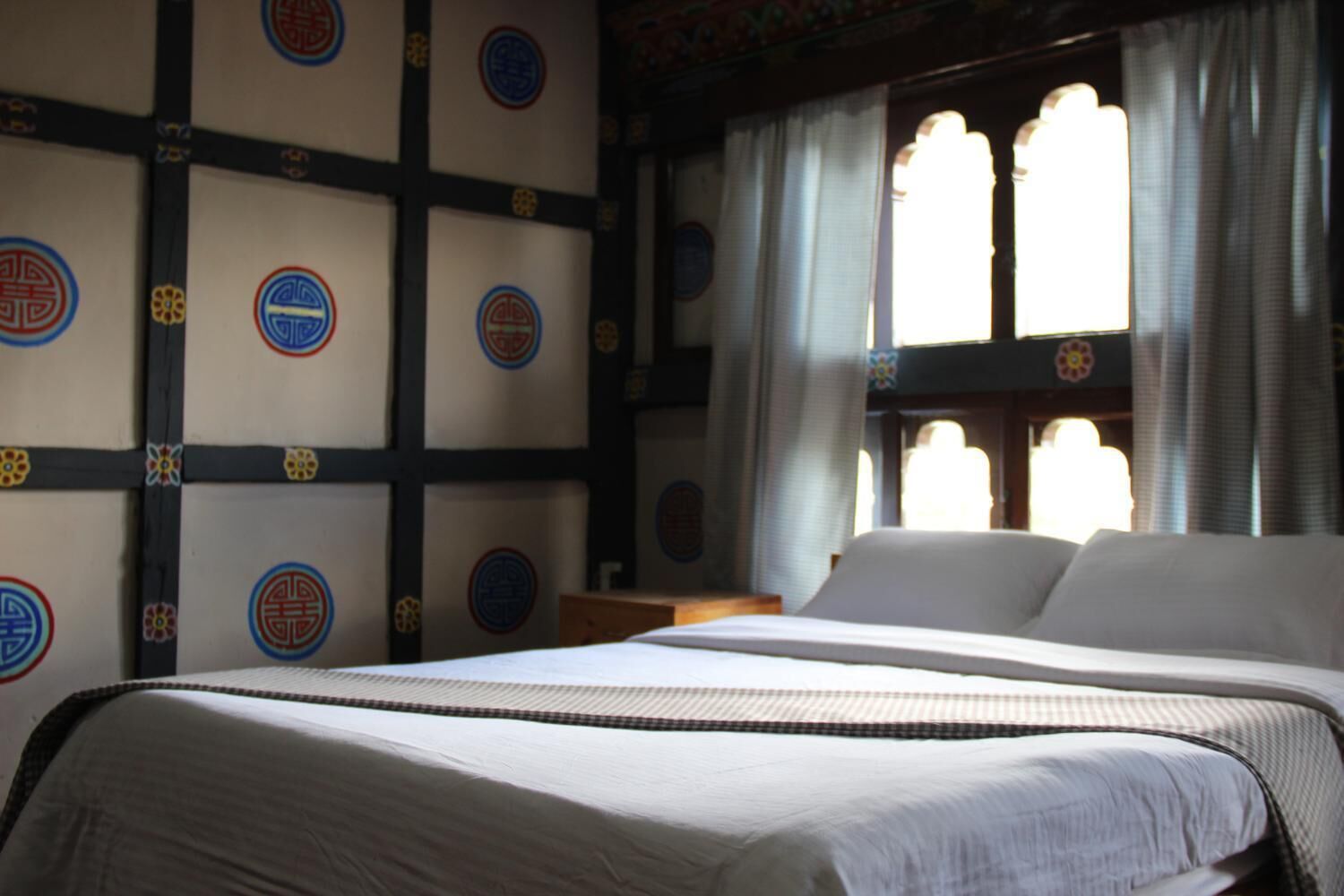 A bedroom with a large bed, a window with curtains, and a wall with circular patterns.