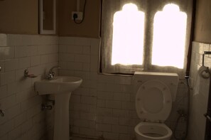 Une petite salle de bain avec un lavabo blanc, des toilettes et une fenêtre avec des rideaux.